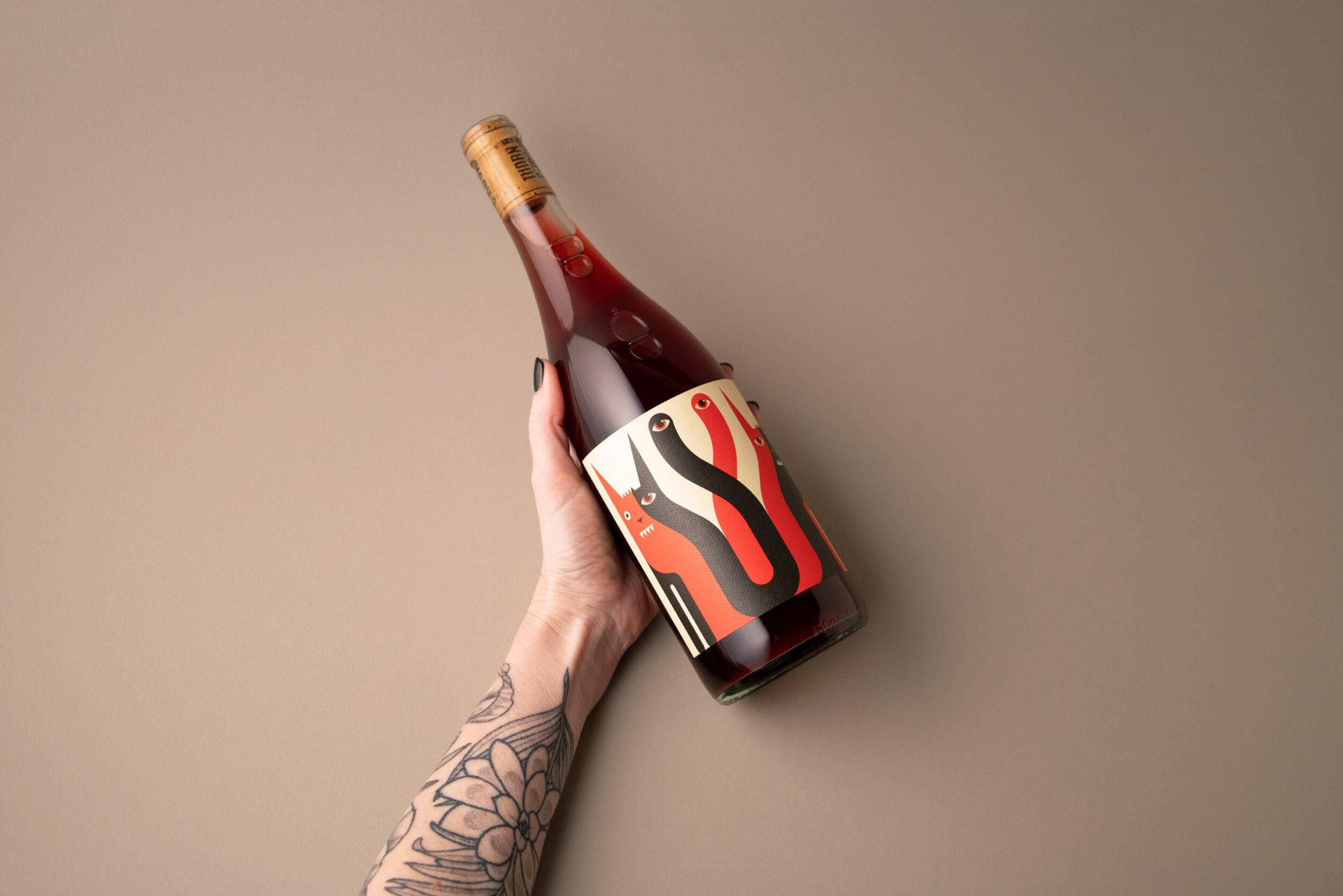 hand holding bottle of shiraz wine, arm has tattoos