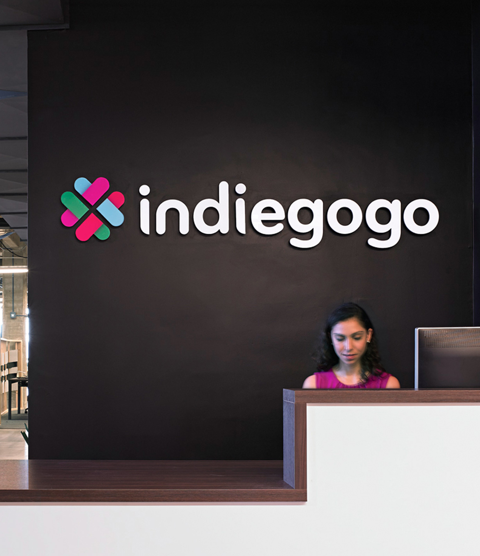 indiegogo offices reception desk with people working at table and logo signage on wall