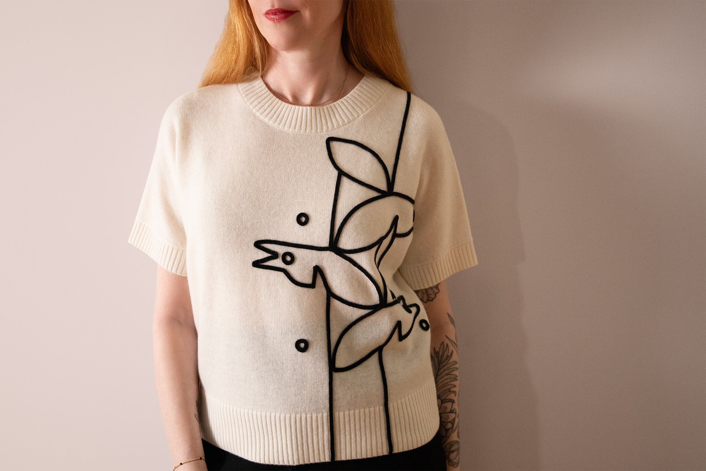 red haired woman wearing a cream cashmere sweater with black crows applique design