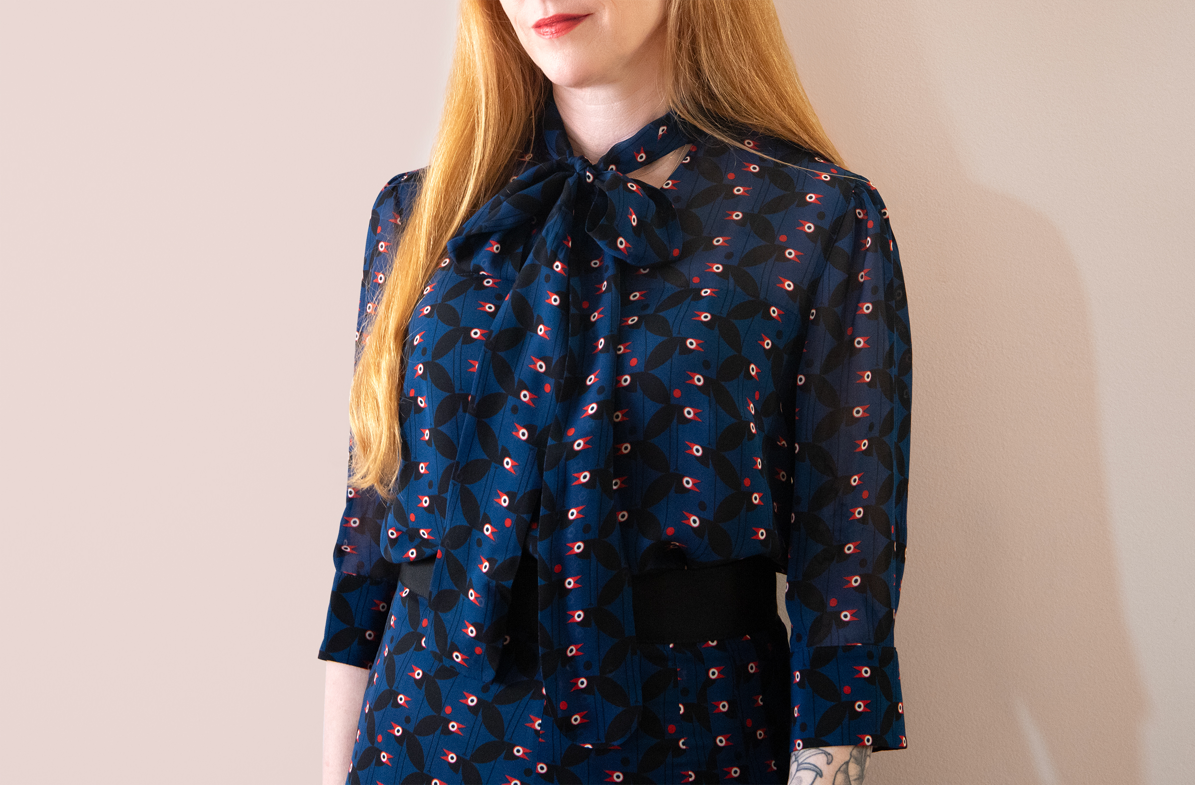 red haired woman with red lipstick wearing a pussy bow blouse and skirt in navy blue with crows pattern in black, white