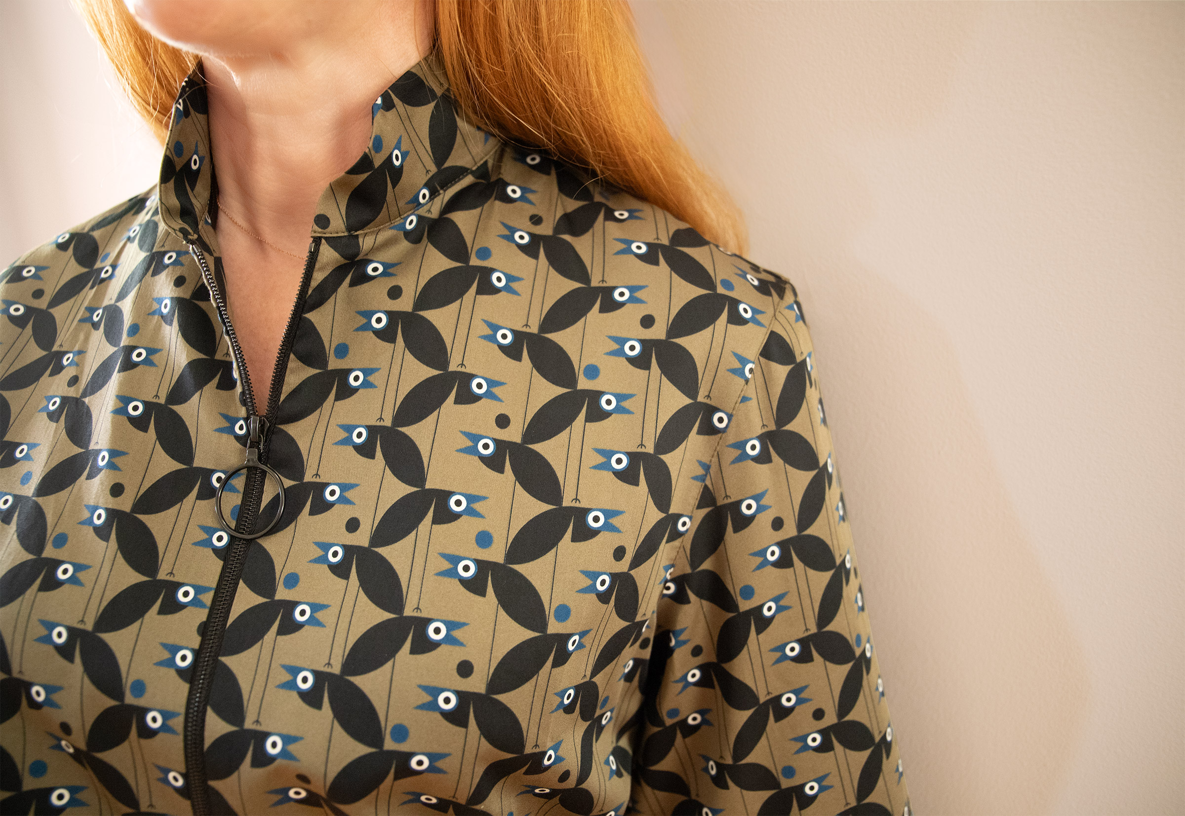 red haired woman close up wearing an olive shirt with zipper front and black and blue crows pattern
