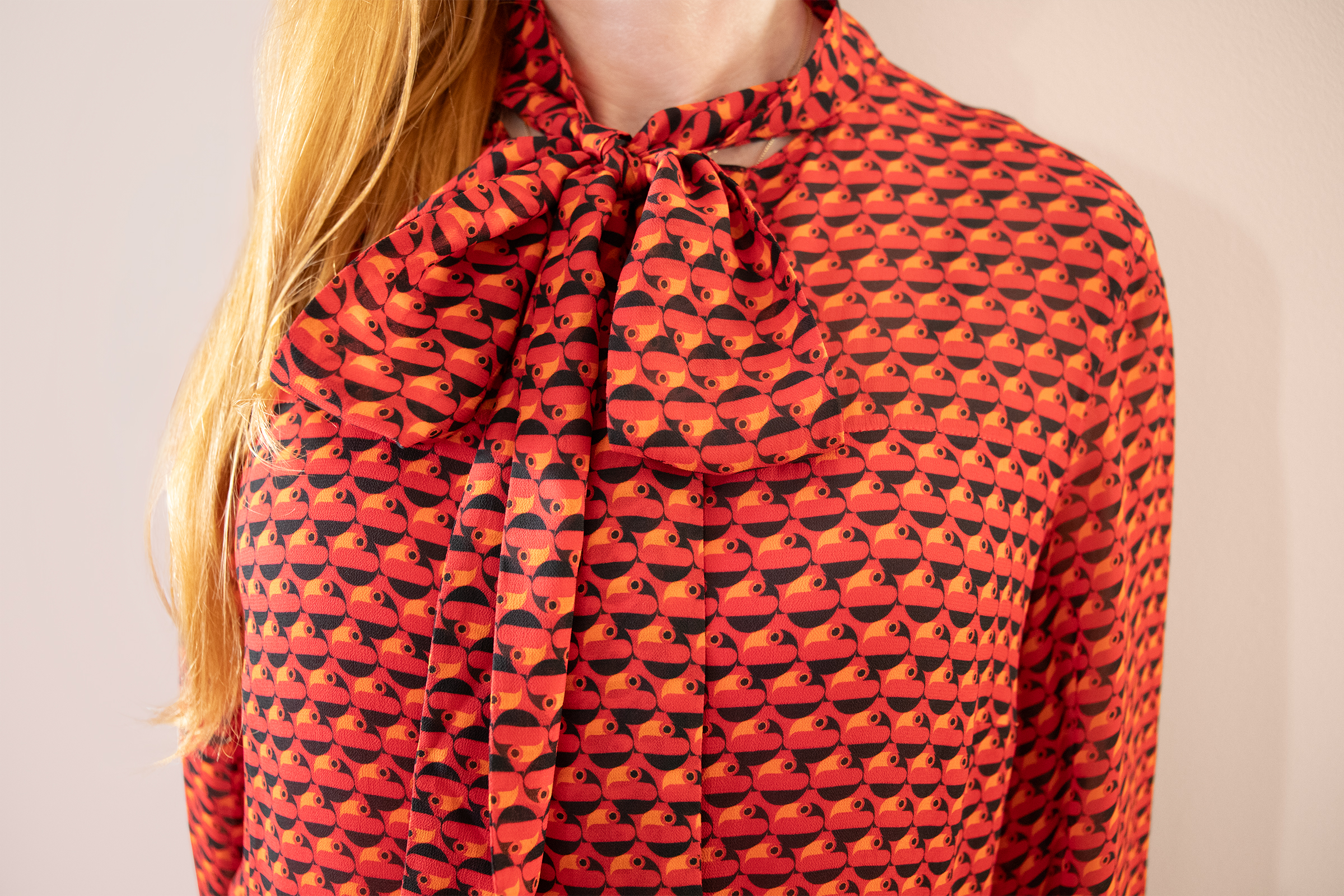 red haired woman wearing a red dress with close up on a bow tie with orange and black bird pattern