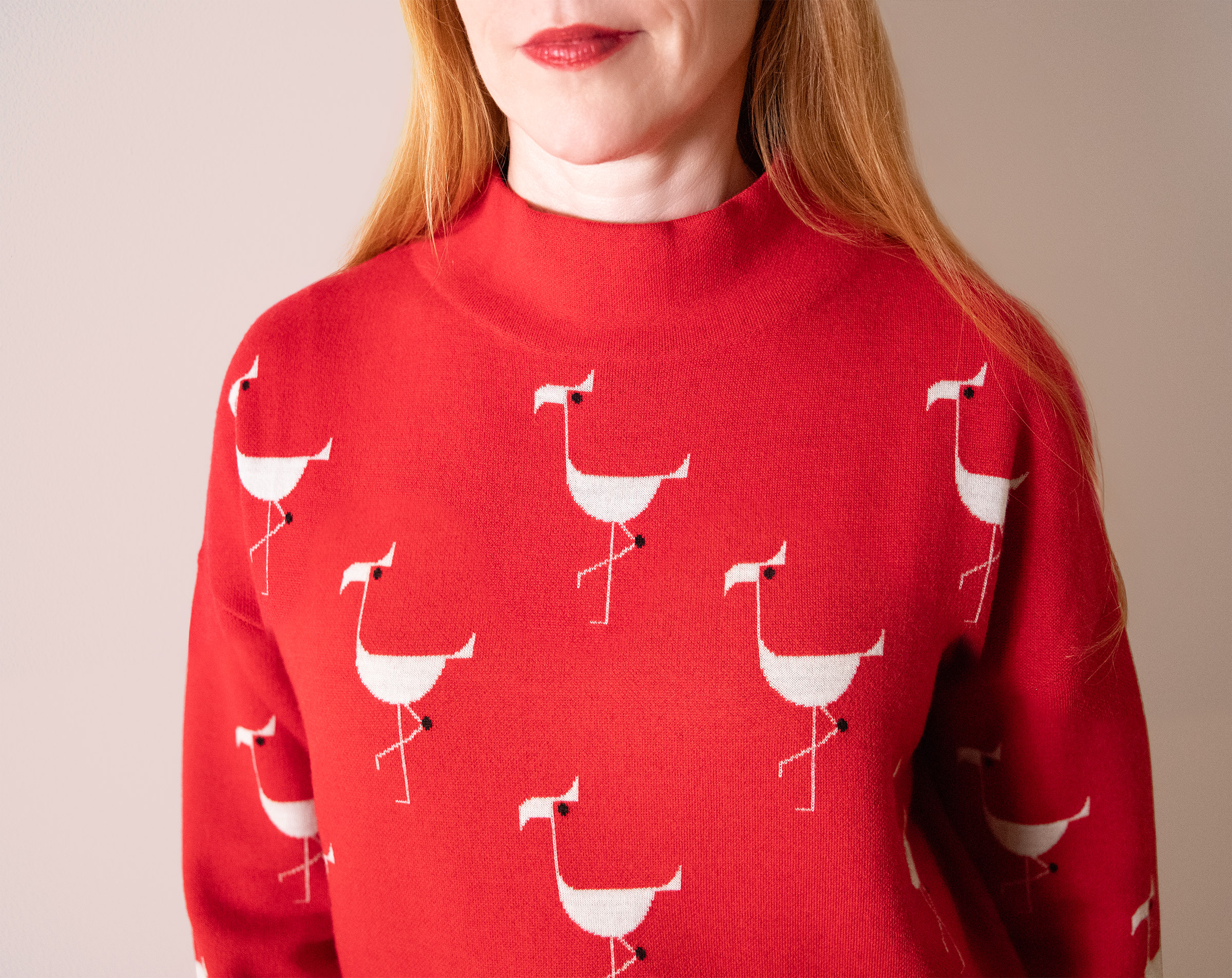 red haired woman with red lipstick wearing a red mock turtleneck sweater with white flamingos