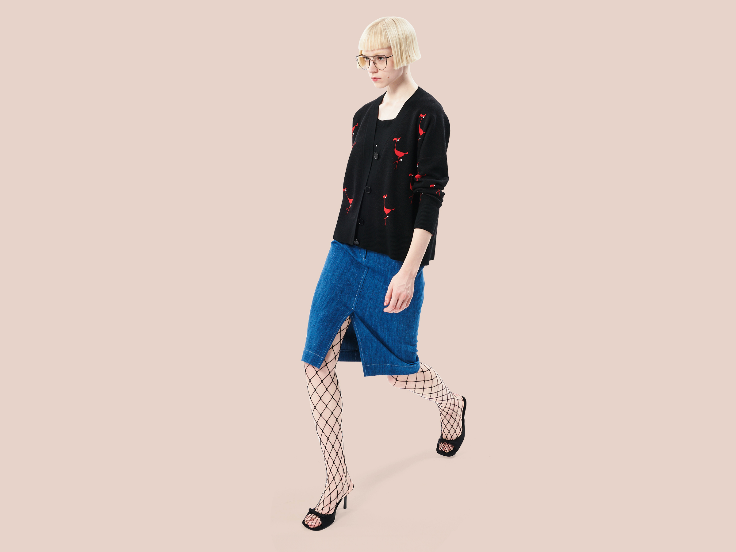 blonde woman with glasses wearing a black cardigan with red flamingos and a denim skirt